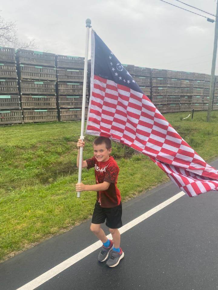 A young boy holding the Flag to Remember flag, proudly above his head.
